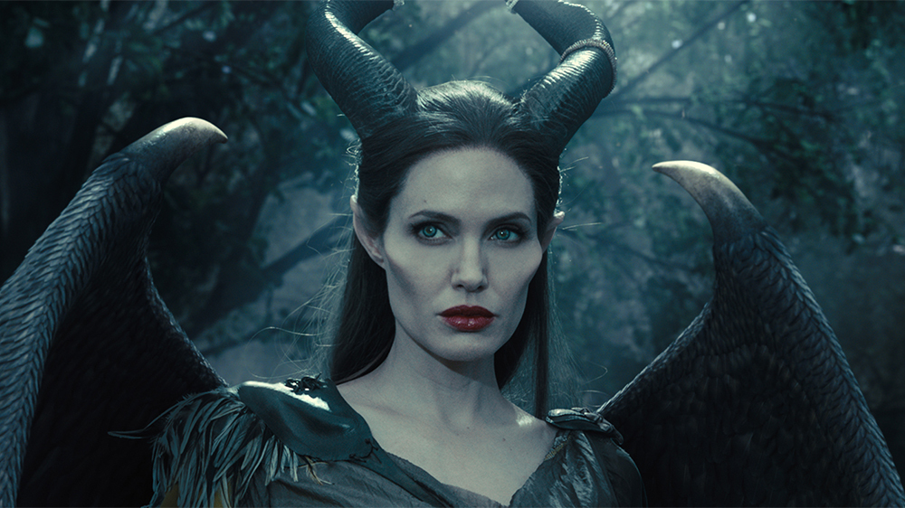 Maleficent (Angelina Jolie), with wings, horns, and enhanced cheekbones, looks wary in closeup in 2014’s Maleficent